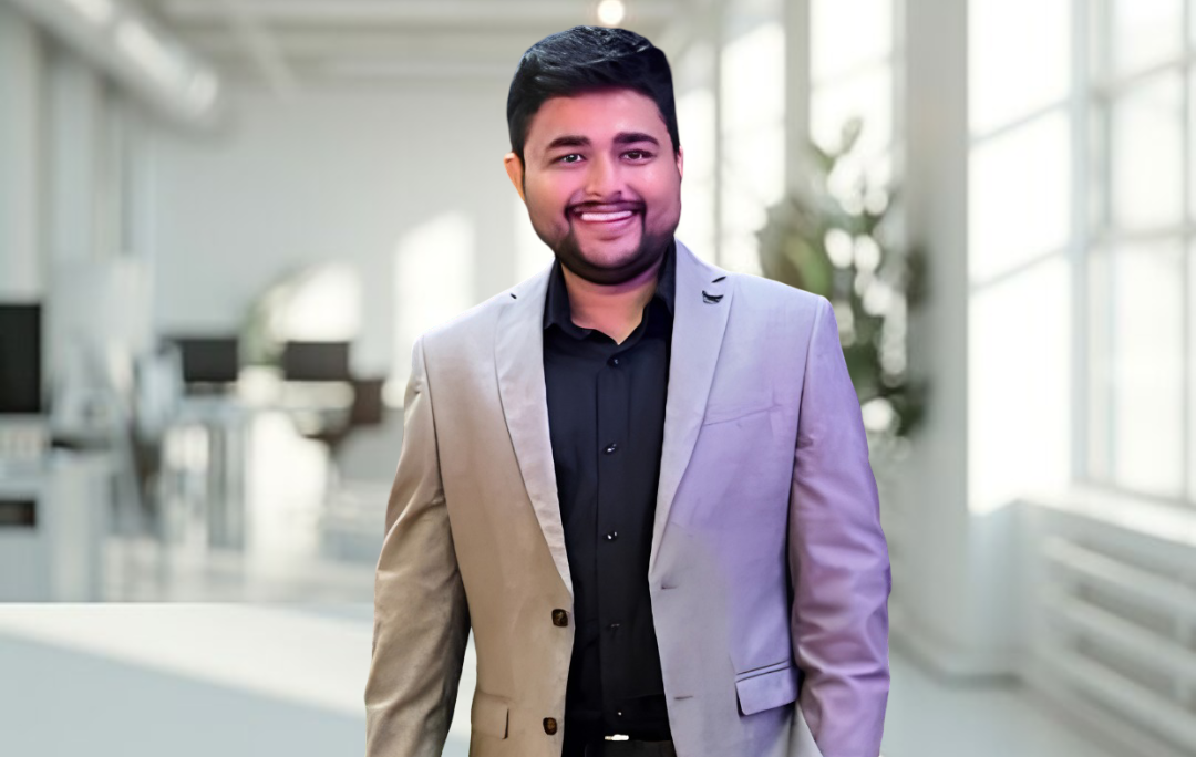 Smiling professional in a suit stands in a bright, modern office, representing a welcoming workplace culture.